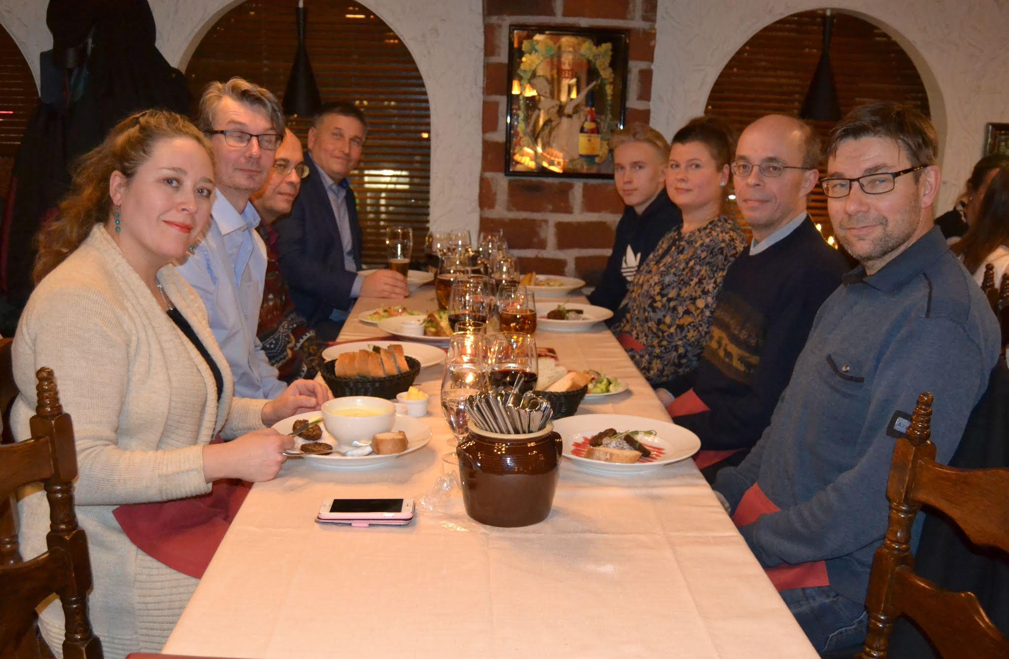 Klubilaiset jouluruokailulla ravintolan pitkän valkoisen pöydän ääressä, taustalla tiiliseinä ja kaari-ikkunat, 21.12.2019