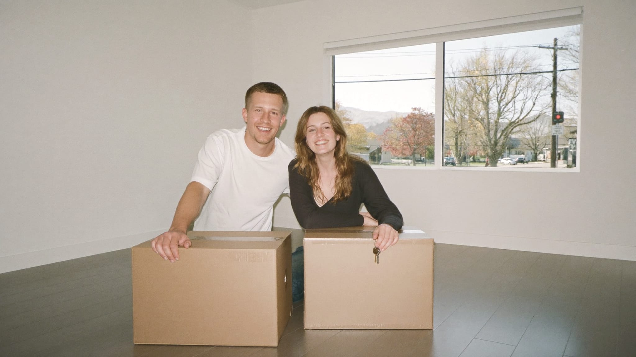 A couple leaning on packed moving boxes in an empty living room