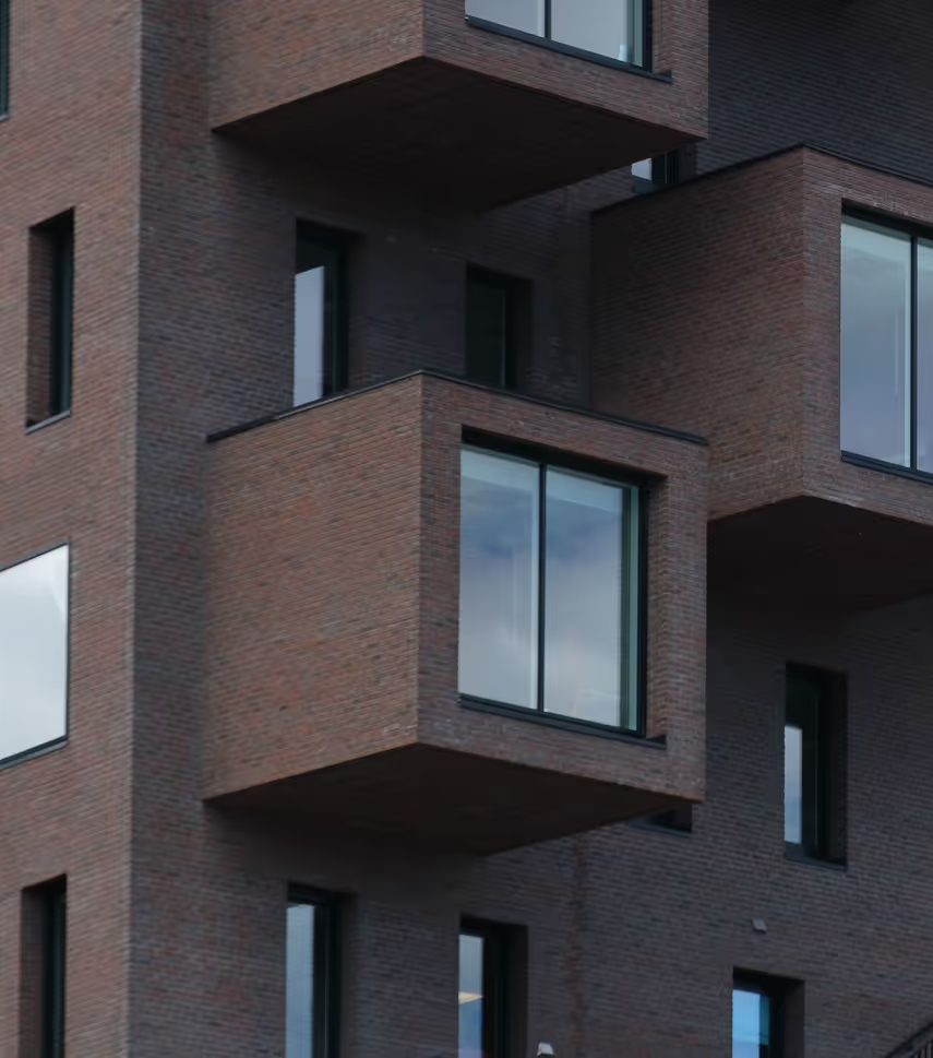 Nærbilde av mursteinsbygning med fremtredende utstikkende balkonger og glassvinduer.