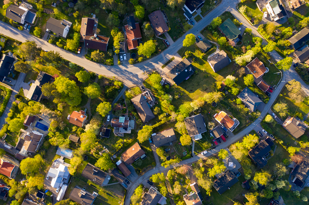 Luftfoto av et boligområde med hus, veier og trær i sollys.