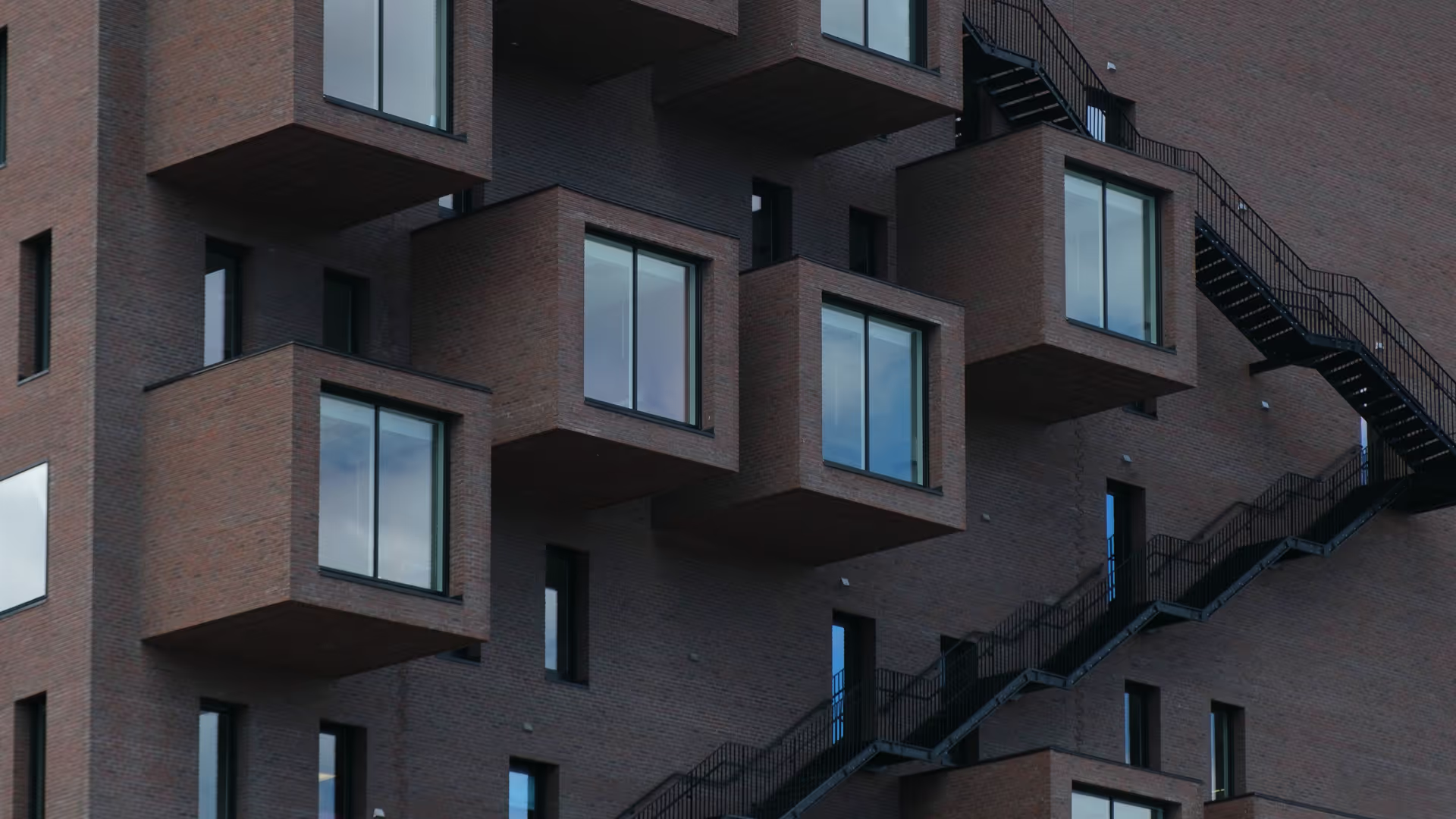 Moderne bygning med fremtredende, utstikkende firkantede vinduspartier i murstein og utvendig sort metalltrapp.