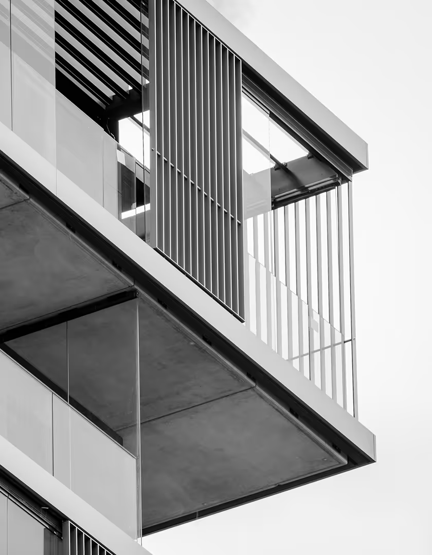 Nærbilde av moderne bygningsfasade med glassrekkverk og metallpersienner i svart-hvitt.