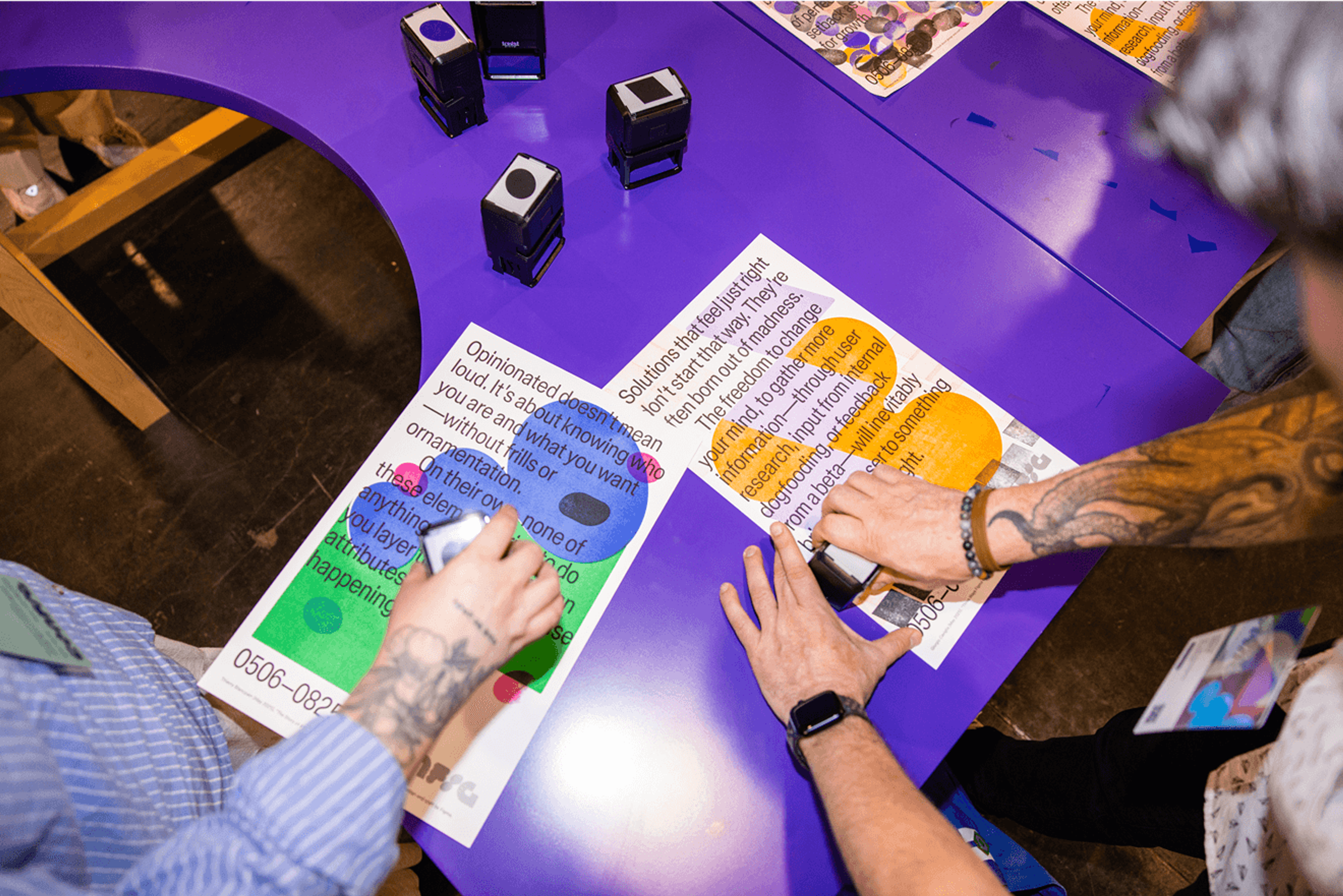 Hands stamping colorful poster designs on a purple workshop table.