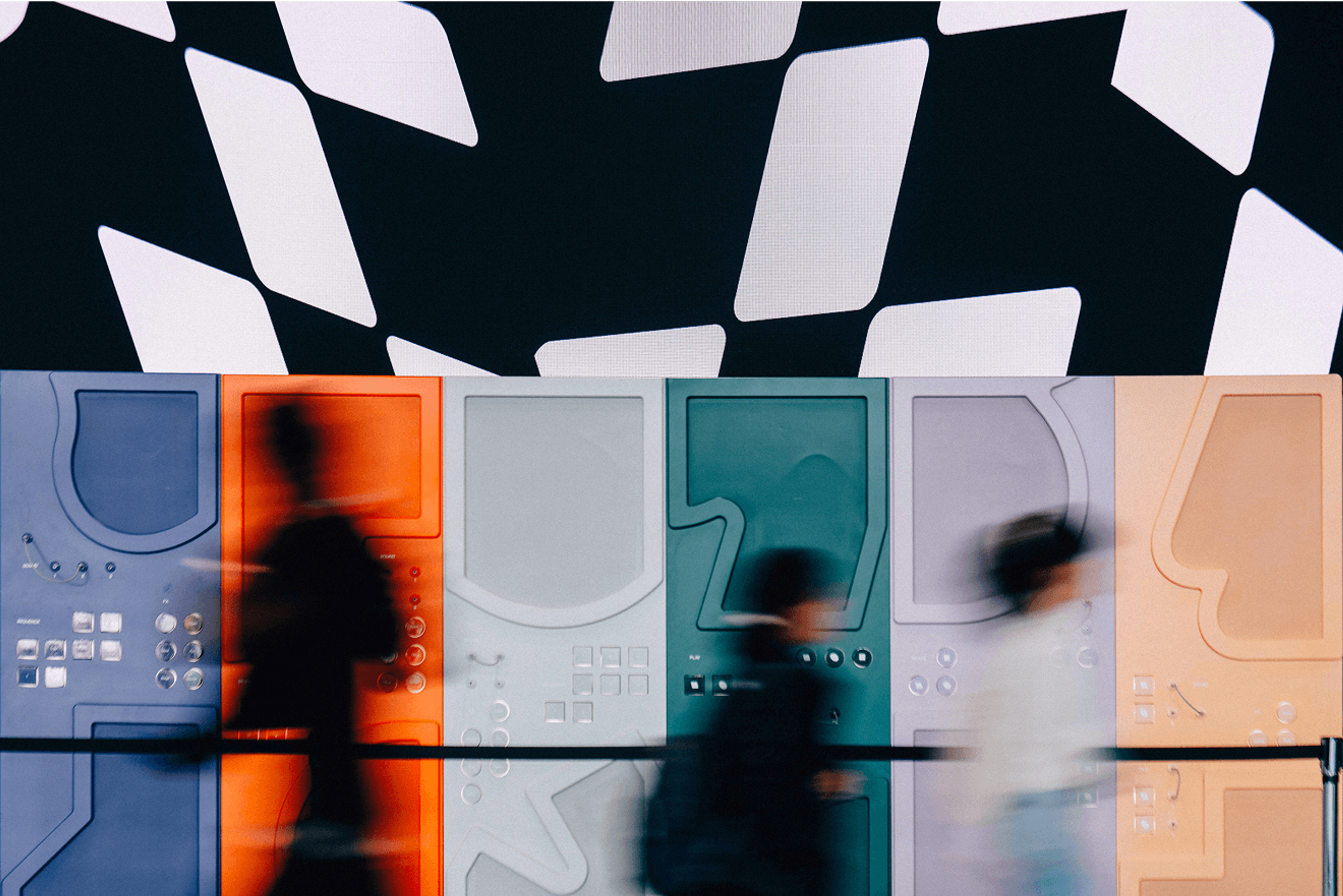 Blurred figures walking past a colorful wall installation with abstract panels and patterns.