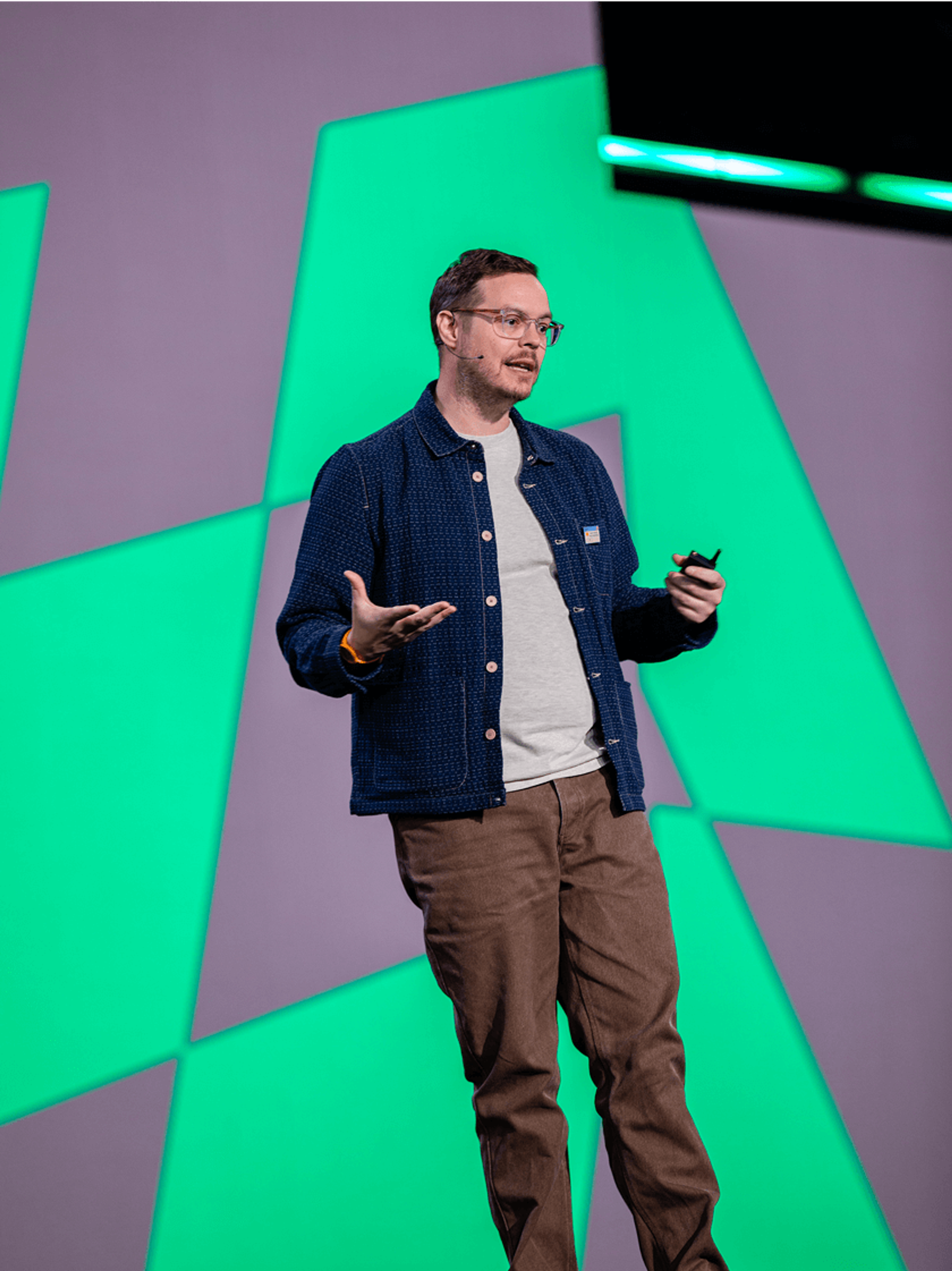 Speaker presenting on stage with a bright green geometric backdrop.