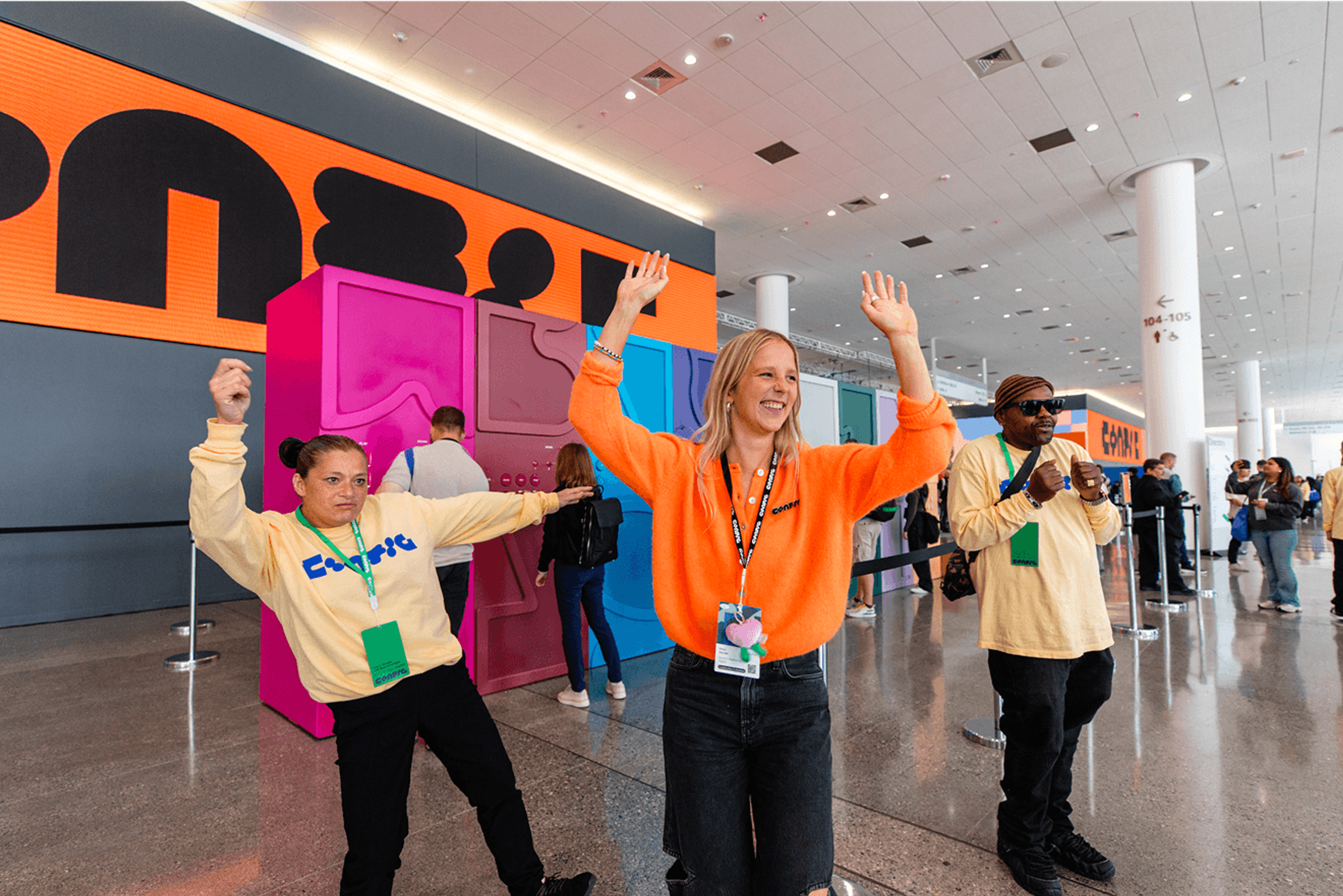 Event staff dancing and raising their hands in front of a bright orange Config sign inside the venue.