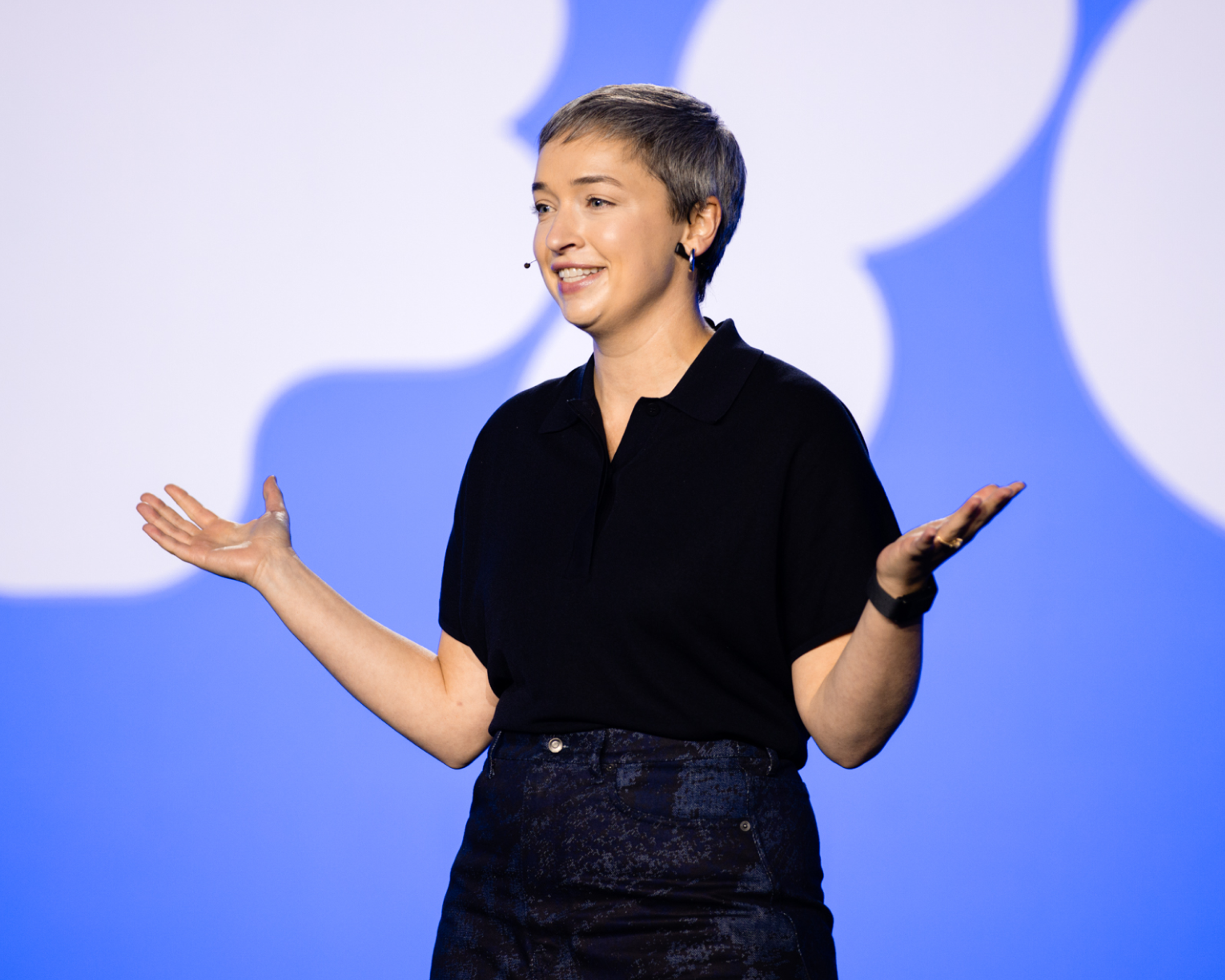 Speaker on stage at Figma Config 2025, smiling with arms open in front of a blue and white backdrop.