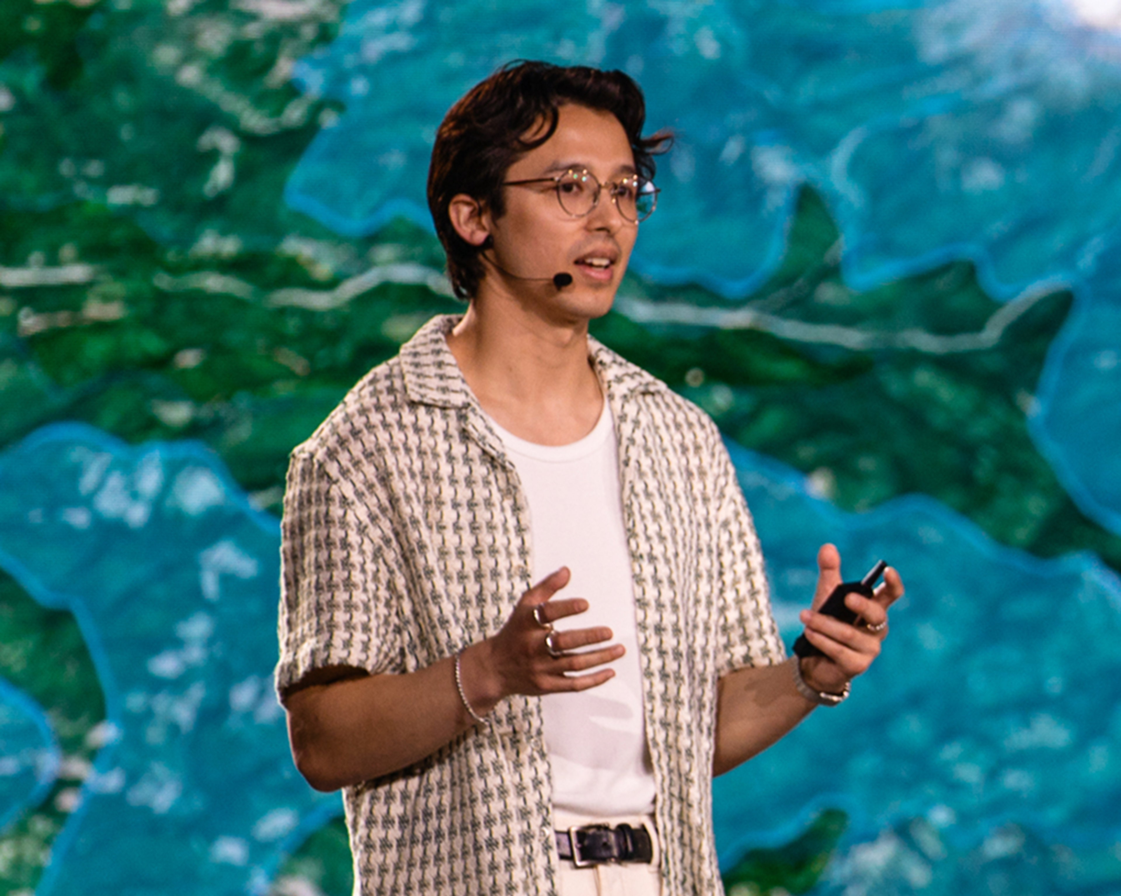 Speaker with tan and white pattern shirt in front of a blue and green background