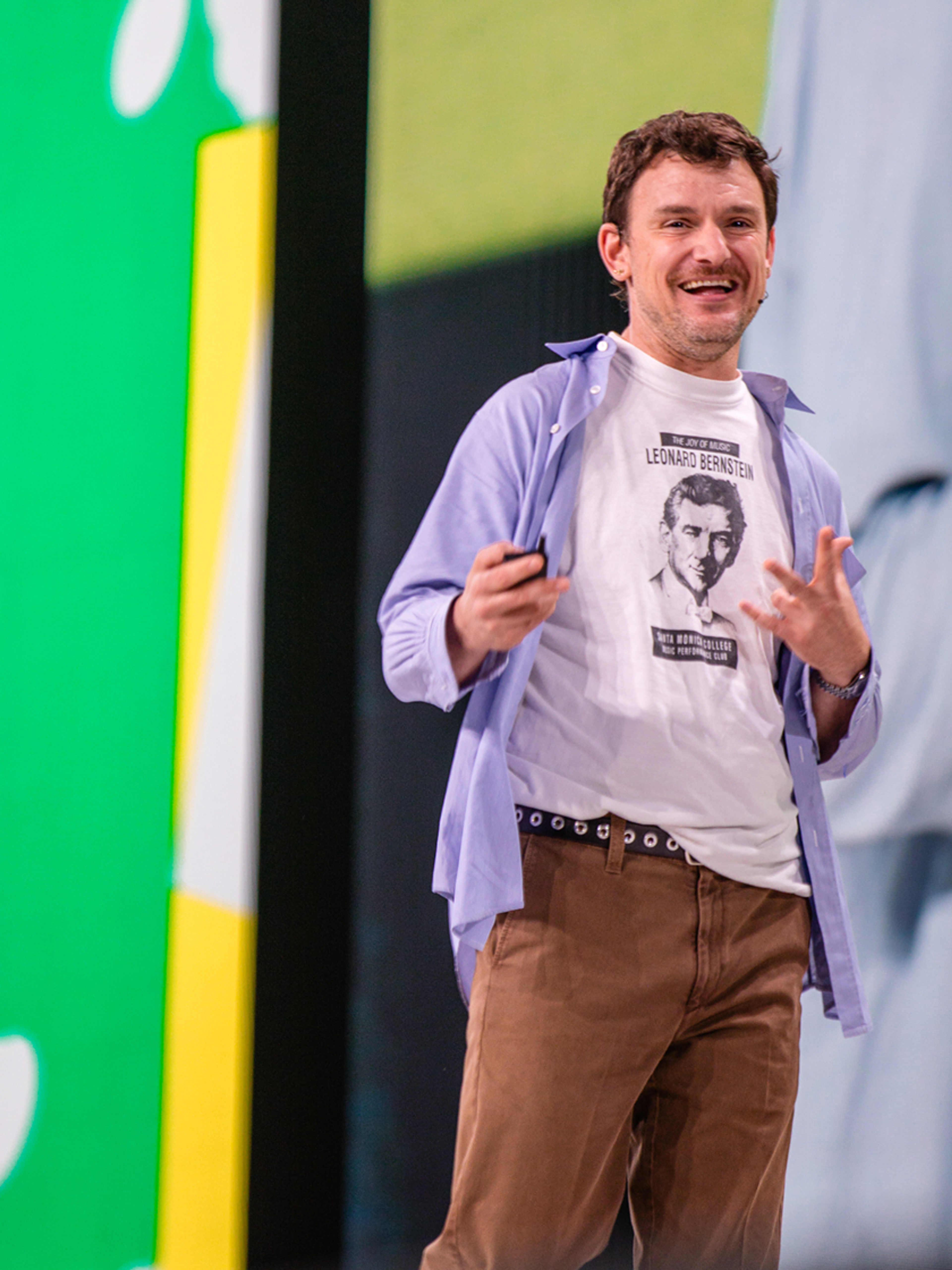 Speaker presenting on stage with a bright green geometric backdrop.
