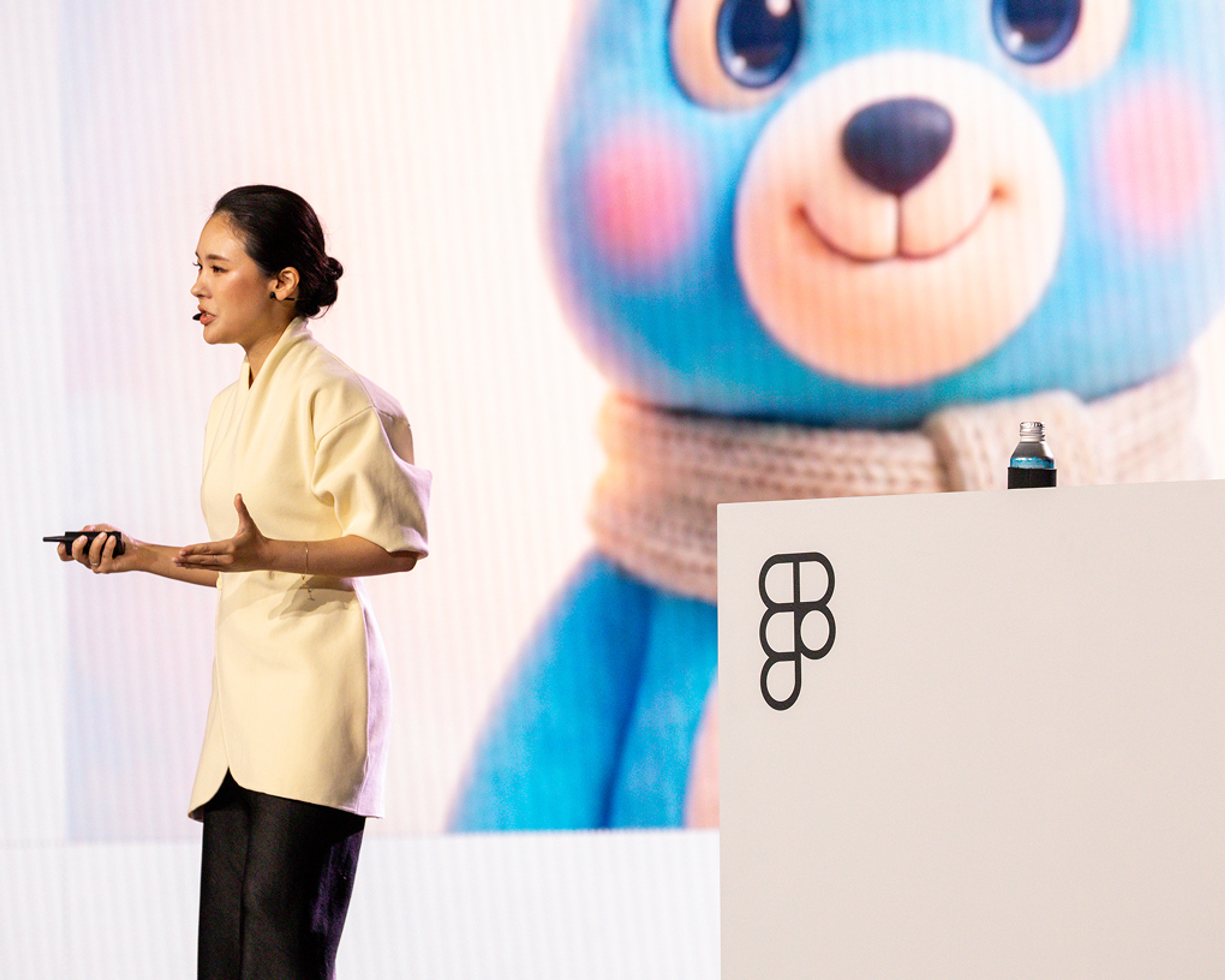 Speaker on stage at Figma Config 2026, telling their story with an animated blue bear on the screen in the background.