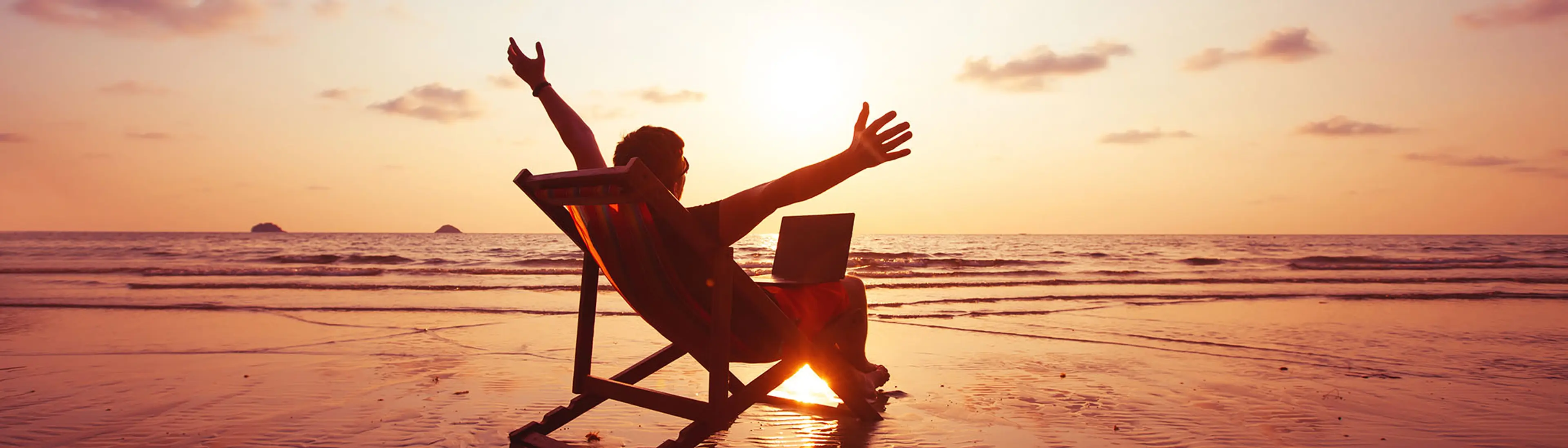 Mann på stranda med laptop i solnedgang