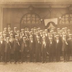 Foto: Foto i Mandskorets eie. Haugesund Sangerforbund 17 mai ca.1920. utenfor Festiviteten. I midten (1.rekke tv) ser vi Søren Nymann, en av Mandskorets stiftere. Han sluttet som sanger i nov. 1921, og ble korets første æresmedlem i Mandskoret i 1922. Festiviteten ble innviet i mai 1920.