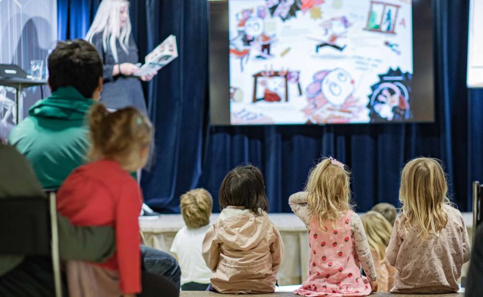 Barn sitter på benk og hører på forfatter på Søndagsbarn.