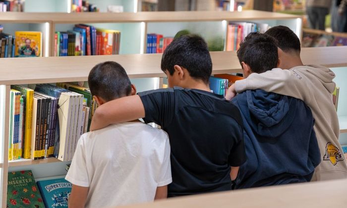 Fire unge gutter står ved en bokhylle på et bibliotek og ser på bøkene. Foto: James Chanika.