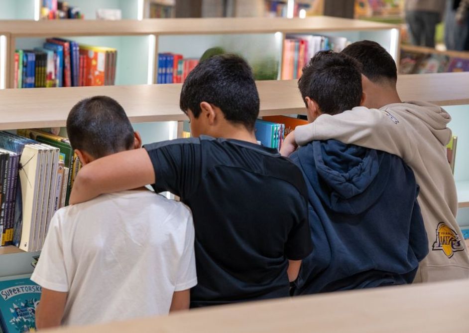 Fire gutter står foran en bokhylle og holder armene rundt hverandre.