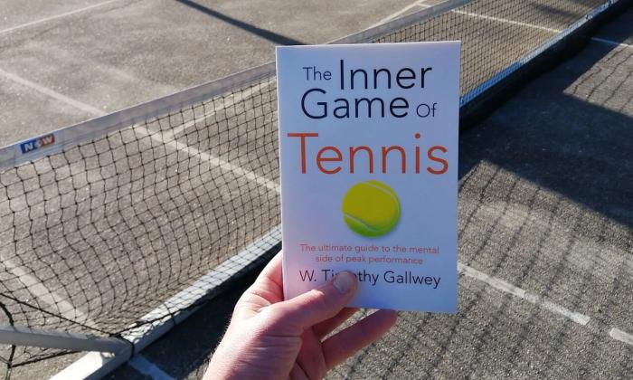 The inner game of tennis holdt i en hånd foran tennisnett