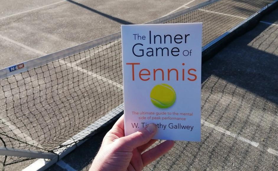 The inner game of tennis holdt i en hånd foran tennisnett