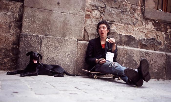Skateren Ali Boulala sitter på skateboardet og spiser. Ved siden av han ligger hunden hans