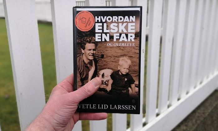 Hvordan elske en far og overleve av Vetle Lid Larssen holdt foran et gjerde