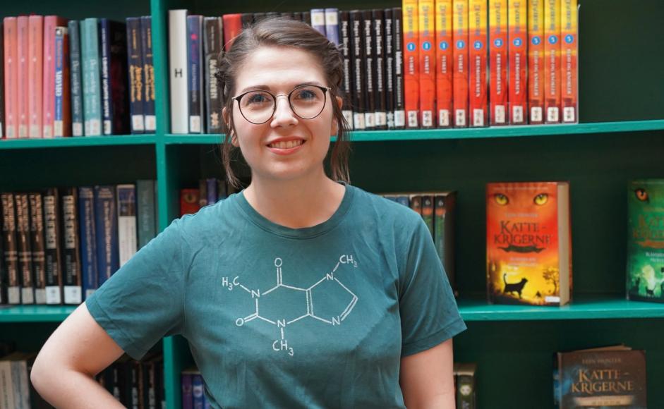 Sofie Birgitte Andersen ser i kamera foran en bokhylle med bøker.