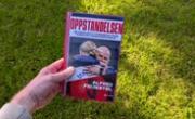 Boka Oppstandelsen av Alfred Fidjestøl holdt foran en gressplen