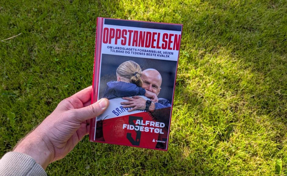 Boka Oppstandelsen av Alfred Fidjestøl holdt foran en gressplen