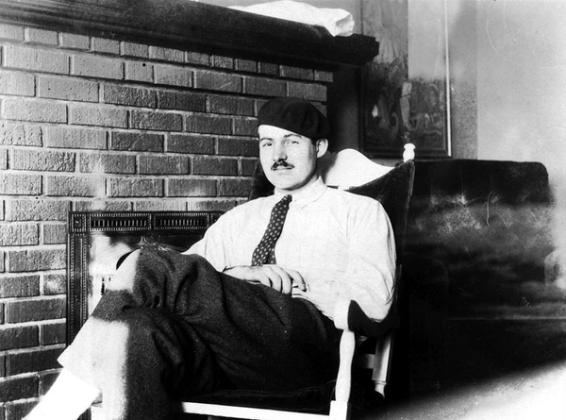 Ernest Hemingway sittende i en stol med lue på