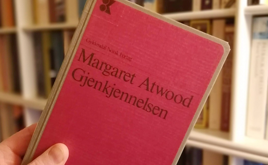 Boka Gjenkjennelsen av Margaret Atwood holdt foran bokhylle