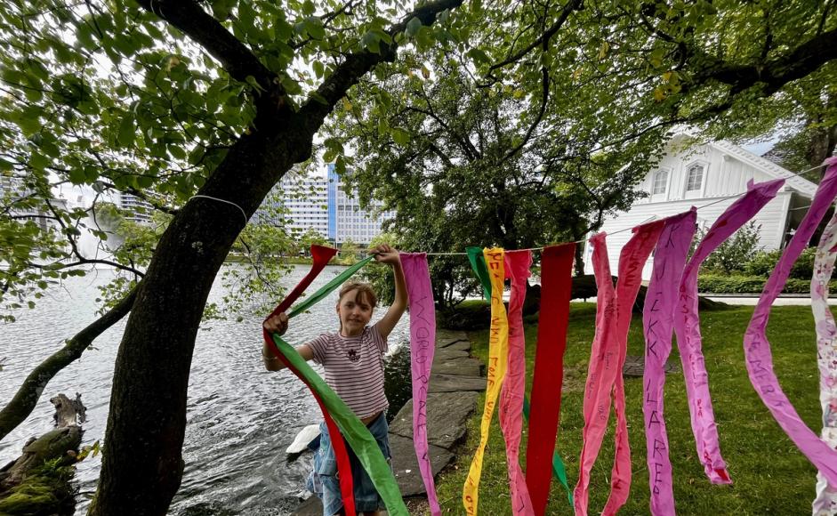 En jente henger opp tøyremser med ønsker for framtiden i trær ved Breiavannet.