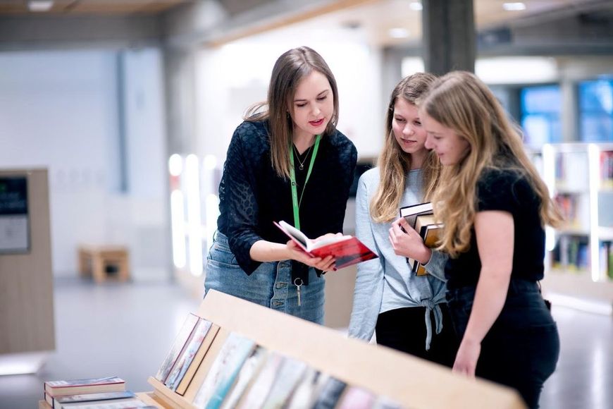 Bibliotekar Ingunn Øvrebø viser bøker til to tenåringsjenter