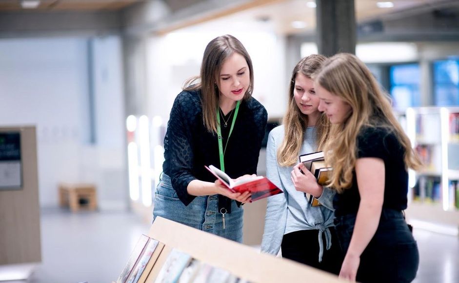 Bibliotekar Ingunn Øvrebø viser bøker til to tenåringsjenter