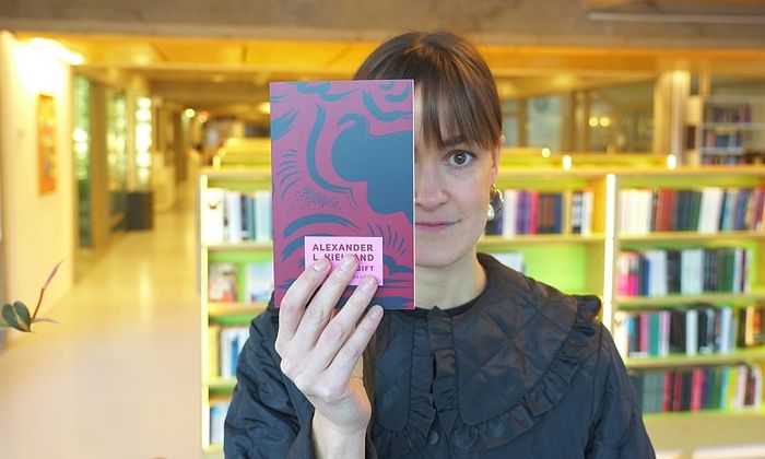 Alvilde Tobiassen holder boka Gift av Alexander Kielland foran ansiktet i Sølvbergets andre etasje