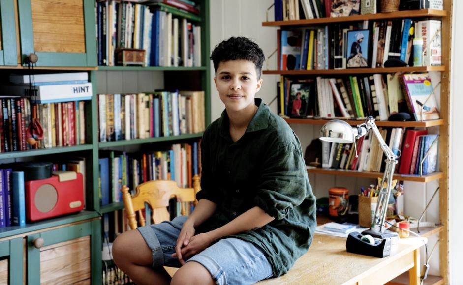 Marjam Idriss sitter på en skrivepult. Rundt henne er det bokhyller med mange bøker. 