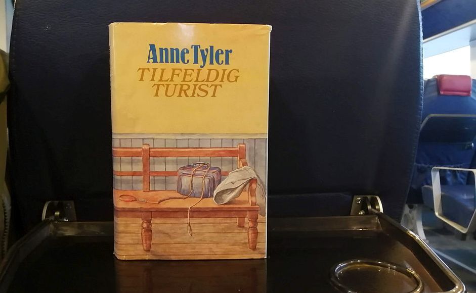 Tilfeldig turist av Anne Tyler bok stående på et brett i båt med et blått setetrekk foran