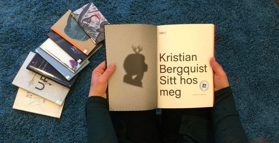 Person som leser i bok av Kristian Bergquist med bøker på gulvet ved siden av