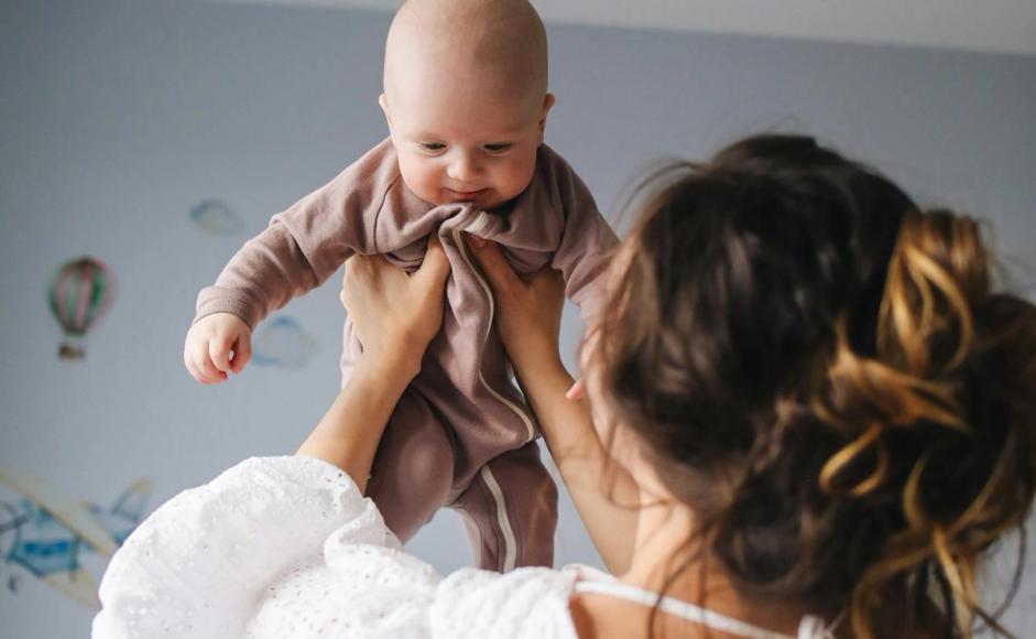 En baby løftes opp på babydans av en dame med ryggen til kamera.