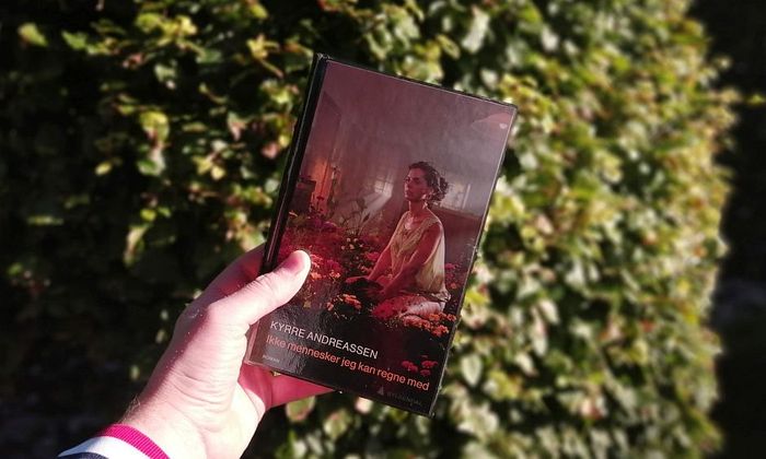 Boka Ikke mennesker jeg kan regne med av Kyrre Andreassen holdt foran et tre