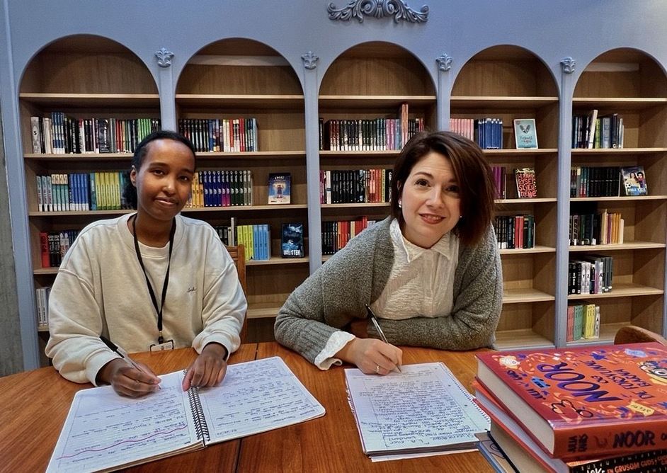Mulki Mukhtar Mohamud Osoble og Sofie Birgitte Andersen sitter ved et bord i biblioteket og skriver.