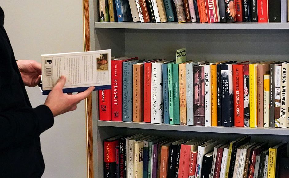 Hender som holder bok foran bokhylle