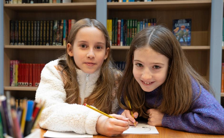 Bilde av to jenter skriver fortellinger i biblioteket.