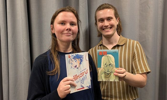 Einar Hildonen og Mette Henriksen holder mangabøker foran grå gardin