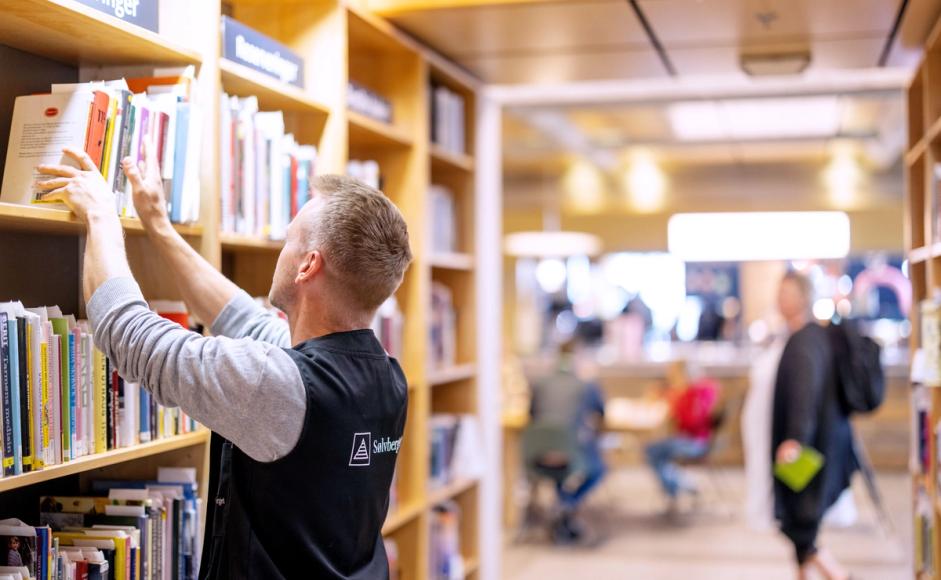 Foto av ansatt som rydder i hyllene på biblioteket.