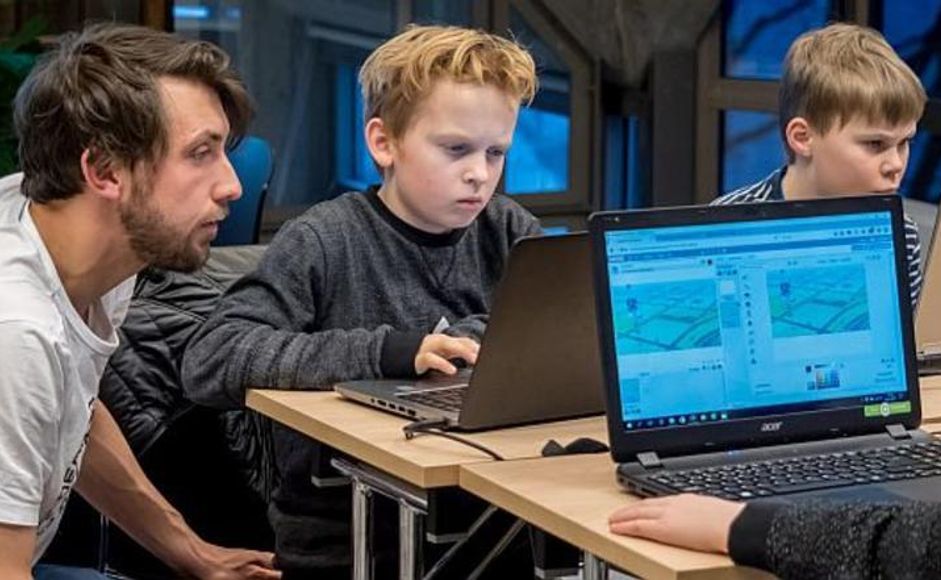 Stemningsbilde fra kodeklubb. Barn og veileder programmerer på datamaskin.