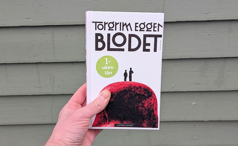 Boka Blodet av Torgrim Eggen holdt foran en vegg