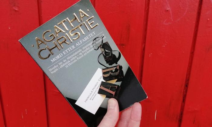 Mord etter alfabetet av Agatha Christie holdt opp foran rød vegg