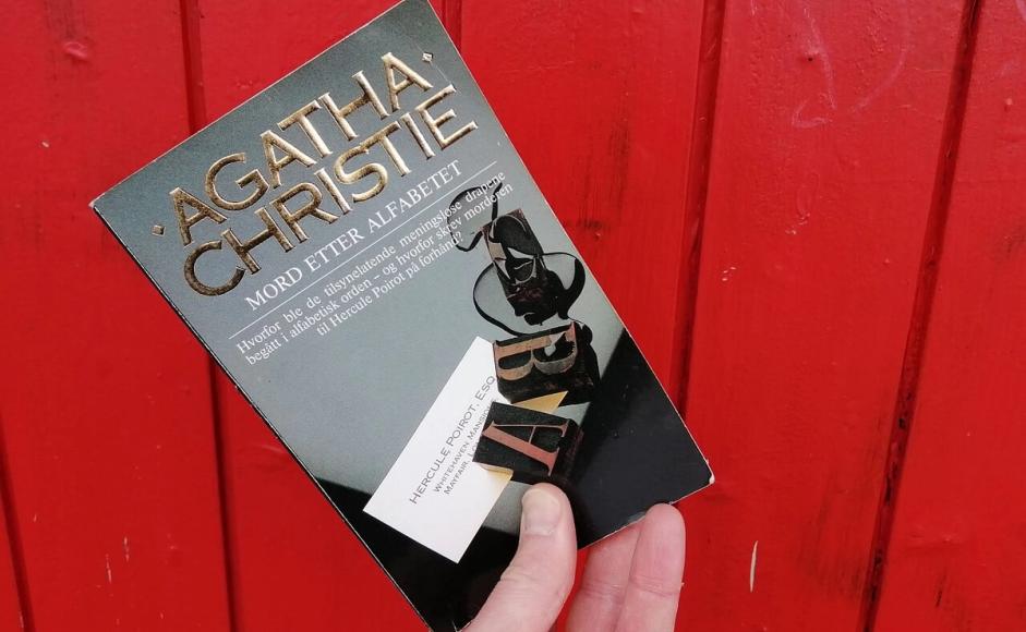 Mord etter alfabetet av Agatha Christie holdt opp foran rød vegg