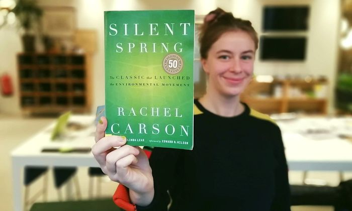 Hannah Ersland holder boka Silent Spring av Rachel Carson mot kameraet i kontorlandskap