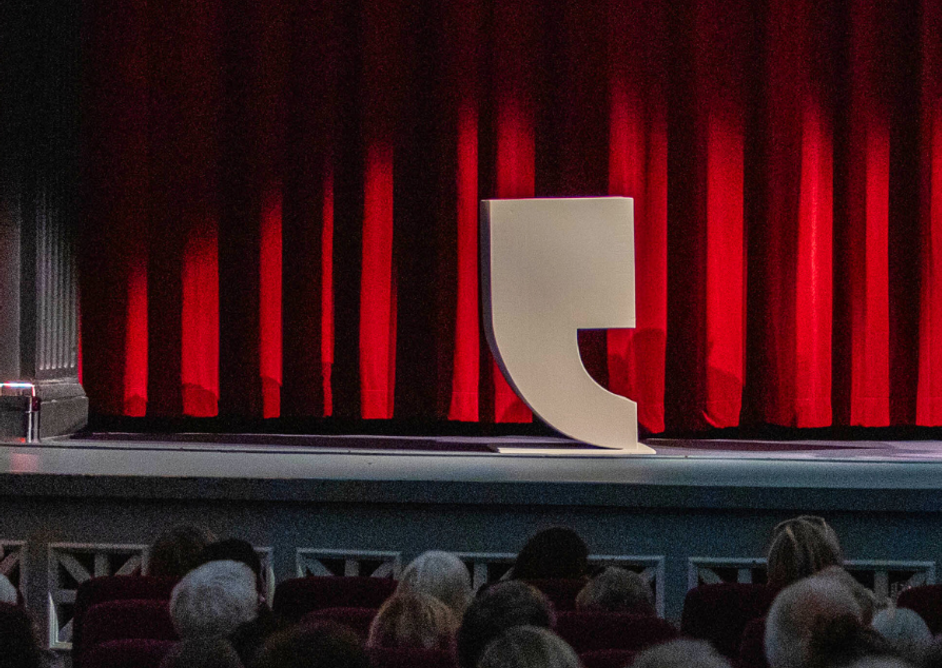 Kapittel-logo stående på en scene med rødt sceneteppe bak