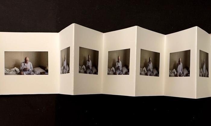 Kunstnerboka "Til Far" eller "Dear Dad" av Anne Tveit Knutsen. Fotografier på hver side av kunstnerens far sittende på en seng. Håndlaget av kunstner og foldet som trekkspillformat.