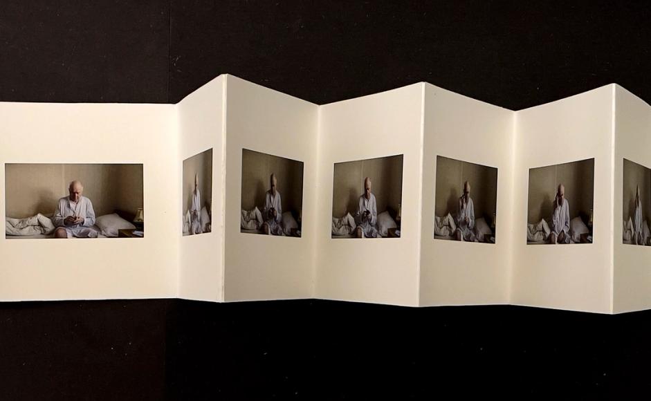 Kunstnerboka "Til Far" eller "Dear Dad" av Anne Tveit Knutsen. Fotografier på hver side av kunstnerens far sittende på en seng. Håndlaget av kunstner og foldet som trekkspillformat.